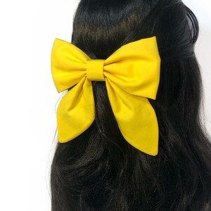 May include: A large yellow bow made of fabric, worn in the hair.
