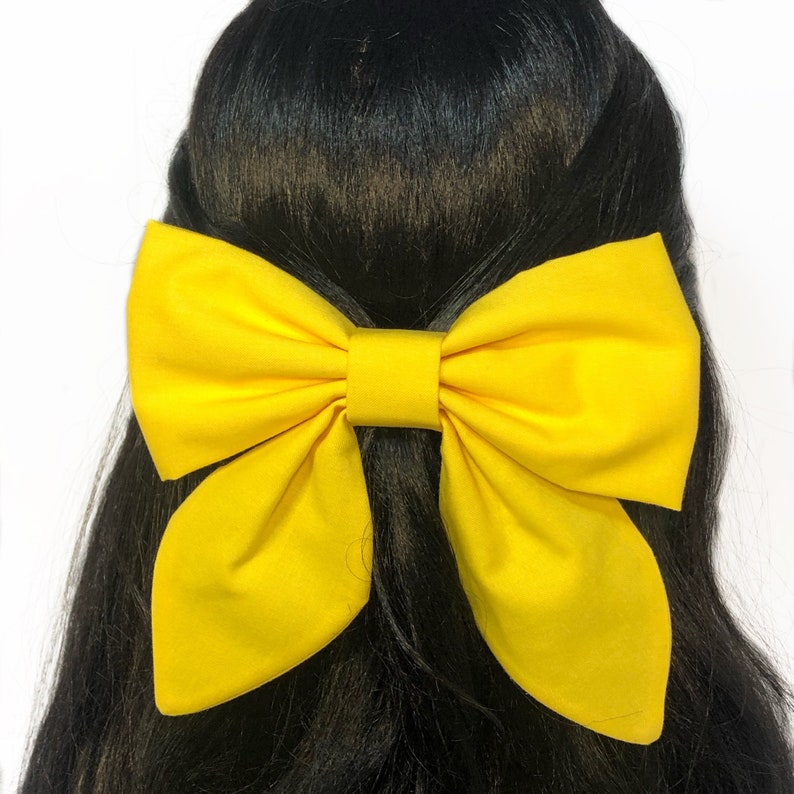 May include: A large yellow bow made of fabric, worn in the hair.