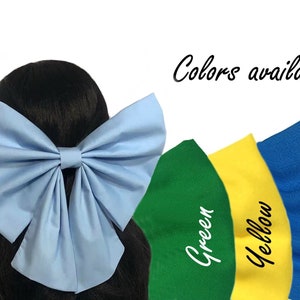 Puede incluir: Un lazo de tela azul claro con un gran nudo de gran tama&ntilde;o. El lazo se muestra en el cabello de una modelo. Colores disponibles: verde, amarillo, azul.