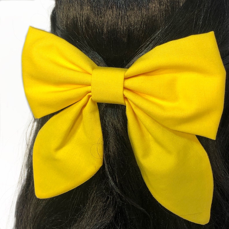 May include: A large yellow fabric bow with a center loop. The bow is tied in a person's hair.