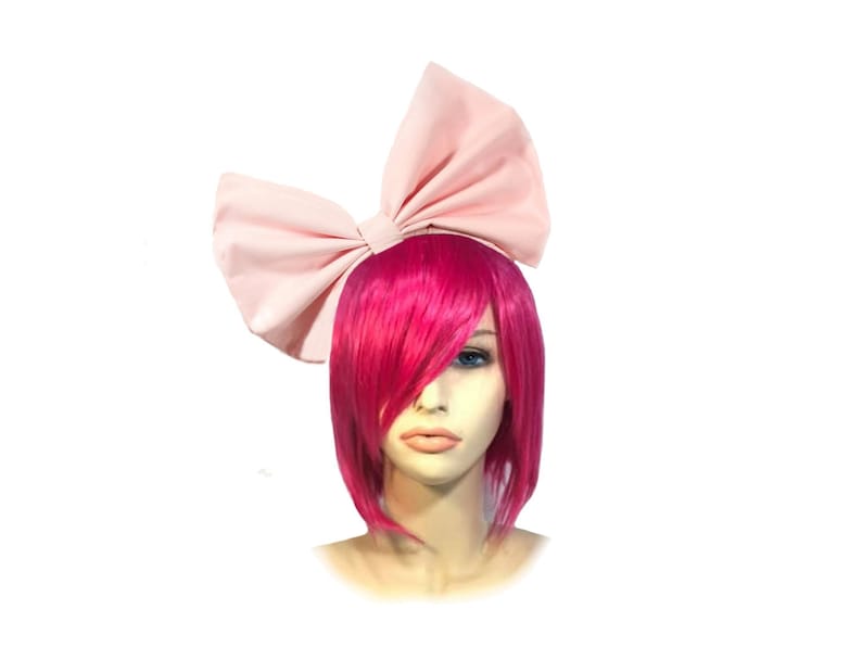 May include: A large pink fabric bow headband. The headband is worn on a mannequin with short, bright pink hair.