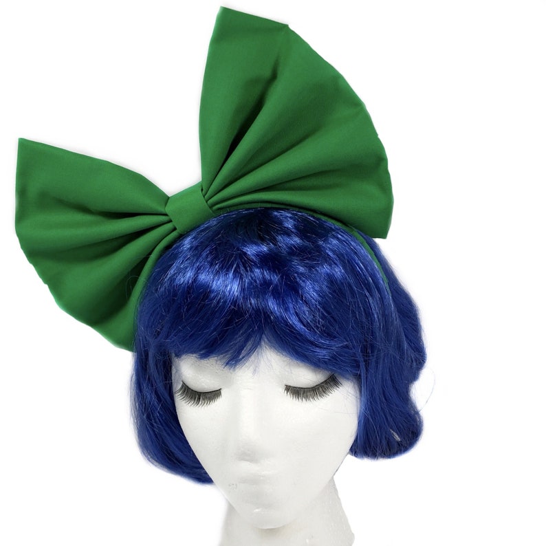 May include: A large green fabric bow headband. The headband is worn on a mannequin with blue hair.