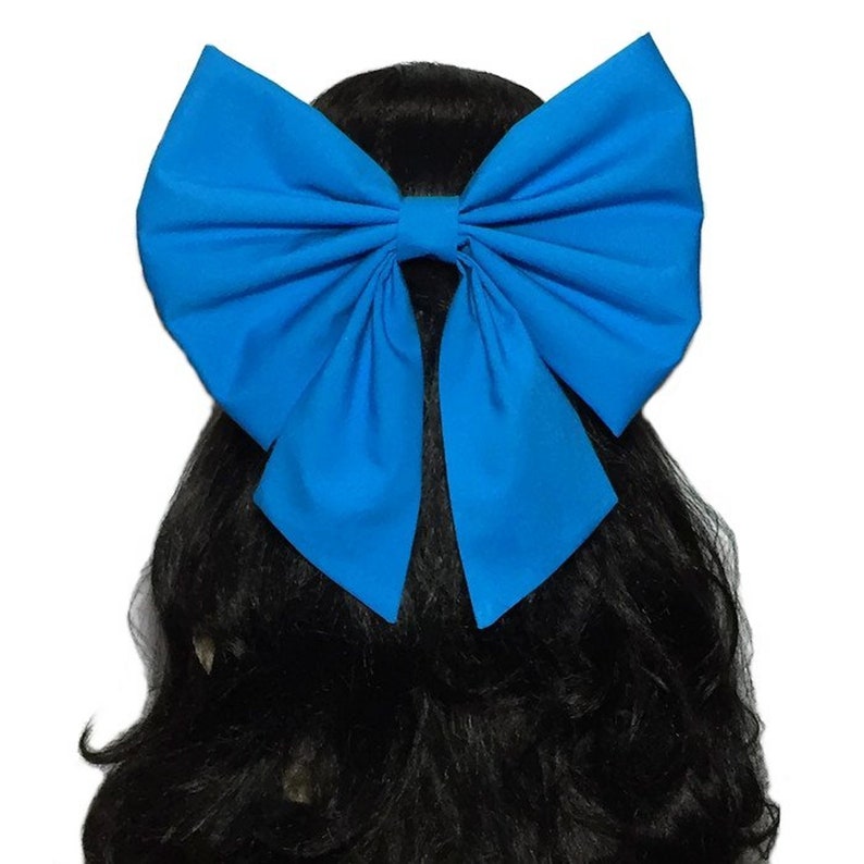 May include: A large, bright blue bow made of fabric. The bow is tied in a classic style with two loops and a centre knot. The bow is worn in the hair.