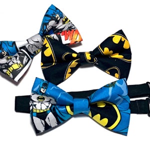 May include: Three bow ties featuring a Batman comic book print. The bow ties are black, blue, and yellow. The bow ties are adjustable with a black elastic strap.