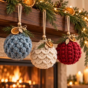 May include: Three spherical ornaments featuring textured crochet patterns in blue, cream, and red. Each ornament hangs from a jute twine loop and is decorated with a dried orange slice, a small wooden leaf cutout, and green pine needles.