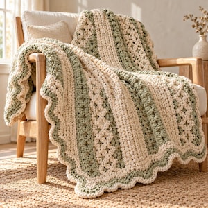 May include: A chunky crochet throw blanket featuring alternating vertical stripes of cream and sage green yarn. The blanket displays a textured pattern with intricate stitch work and a decorative scalloped edge along the border.