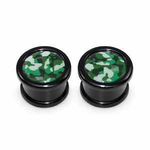 Op de afbeelding: Een paar zwarte oorplugs met een cirkelvormig voorvlak voorzien van een groen, wit en donkergroen camouflagepatroon. De plugs hebben een gladde, glanzende afwerking en een cilindrische vorm met uitlopende randen aan de boven- en onderkant.