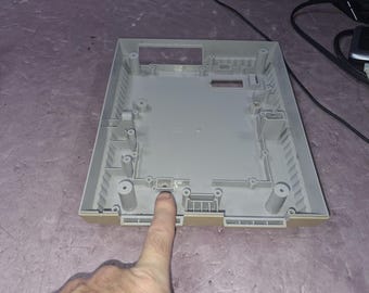 May include: A light gray plastic internal housing shell for a video game console, featuring molded screw posts, rectangular cutouts, and internal structural ribs designed to secure electronic components within the device casing.