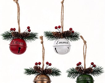 May include: Four round metal jingle bell ornaments in red, white, bronze, and green. Each bell features a jute twine hanger, a sprig of green pine needles, two small pinecones, and red berries. The names Olivia, Emma, Luna, and River are printed.