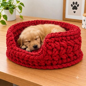 May include: A round, chunky, red crocheted pet bed with thick yarn walls. A golden-colored puppy is curled up and sleeping inside the bed. The bed features a textured, braided knit pattern throughout its circular structure and raised edges.