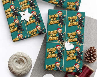 May include: Teal wrapping paper featuring a repeating pattern of a cartoon character wearing a Santa hat, a black suit, and gold sneakers, with the text "TIPTOEING IN MY JORDANS" printed in yellow block letters throughout the design.