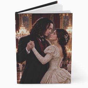 May include: A hardcover journal featuring a printed image of two people in formal attire dancing in a ballroom. The person on the left wears a black suit with a red vest, while the person on the right wears a cream-colored lace gown.