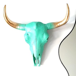 以下が含まれることがあります： ターコイズブルーの雄牛の頭蓋骨に金色の角が付いている。頭蓋骨は壁掛けの装飾品である。