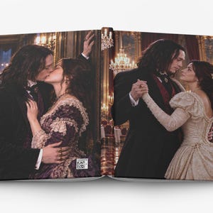 May include: An open hardcover book displaying two distinct scenes. The left side shows a couple kissing in a dark room. The right side shows the same couple dancing in a ballroom. The book cover features a small square QR code with the text 12345678.