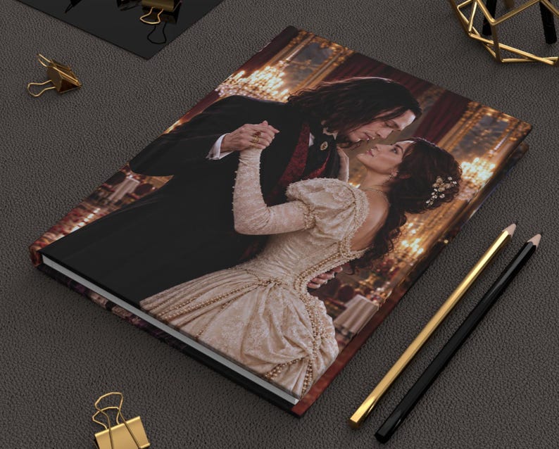 May include: A rectangular hardcover journal featuring a printed image of a couple dancing in a ballroom. The person on the left wears a black suit with a red vest, while the person on the right wears a cream-colored gown with long sleeves.