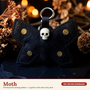 May include: A black felt moth keychain featuring four circular gold accents on the wings and a small white skull centered at the top. The moth is attached to a black fabric loop and a silver metal keyring. The text reads Moth, Felt keychain sewing pattern, a gothic moth with a tiny skull, and PDF INSTANT DOWNLOAD.