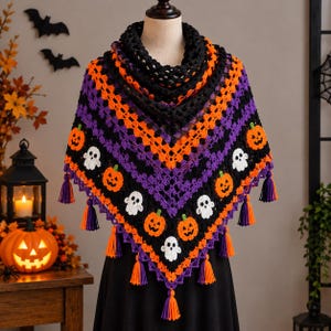 May include: A triangular crochet shawl featuring a repeating pattern of orange pumpkins and white ghosts on a black and purple background. The shawl is finished with a black crocheted collar and multiple orange and purple yarn tassels.
