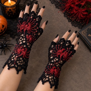 May include: A pair of black fingerless gloves featuring an intricate crochet lace pattern and vibrant red spider lily floral motifs. The gloves extend to the mid-forearm and have a scalloped edge at the wrist and finger openings.