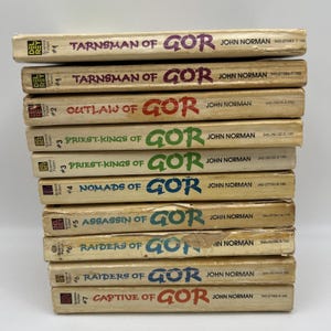 May include: A stack of ten mass-market paperback books from the Gor series by John Norman. The spines are off-white with colored text including Tarnsman of Gor, Outlaw of Gor, Priest-Kings of Gor, Nomads of Gor, Assassin of Gor, Raiders of Gor, and Captive of Gor.