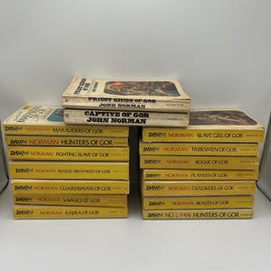 May include: A collection of mass-market paperback books from the Gor series by John Norman, published by DAW Books. The stack includes titles such as Priest Kings of Gor, Captive of Gor, Marauders of Gor, and others, all featuring yellow spines.