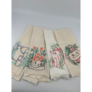 May include: Four off-white kitchen towels with embroidered designs. One towel features a blue elephant, another has a cup with orange flowers, a third has a red teapot, and the last has a teapot with strawberries.