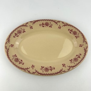 May include: Oval serving platter with a cream-colored center and a maroon floral and scalloped border design. The platter is made of ceramic and is suitable for serving food.