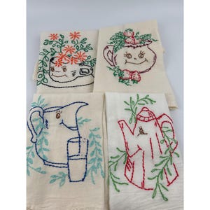May include: Four off-white embroidered kitchen towels. Each towel features a different whimsical design: a teacup with flowers, a teapot with strawberries, a pitcher with a glass, and a teapot with leaves. The embroidery uses red, blue, and green thread.