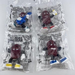 May include: Four Dancin' Raisins collectible figures in individual clear plastic bags. Each brown raisin character features white gloves, black limbs, and colorful sneakers. The packaging displays the Dancin' Raisins logo and graphics.