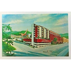 May include: Vintage postcard featuring the Lancer Towers hotel with a red and white facade. A diver is depicted mid-air above a pool. The postcard shows a street view with palm trees and a fountain, set against a backdrop of mountains and a blue sky.