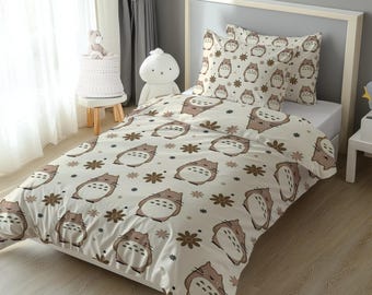 Puede incluir: Un juego de cama que incluye una funda nórdica y una funda de almohada de color crema con un patrón repetitivo de criaturas de dibujos animados marrones y pequeñas flores marrones. La tela muestra un estampado constante de personajes.