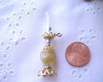 May include: A miniature gold-colored oil lamp with a clear glass chimney and a yellow and white marbled base. The lamp is about the size of a US penny.