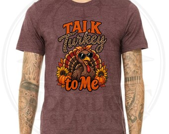 Può includere: Una t-shirt a maniche corte color bordeaux mélange con la grafica di un tacchino che indossa una fascia con stampa leopardata e occhiali da sole. Il tacchino è circondato da girasoli e zucche, con la scritta "TALK Turkey to Me" in arancione.
