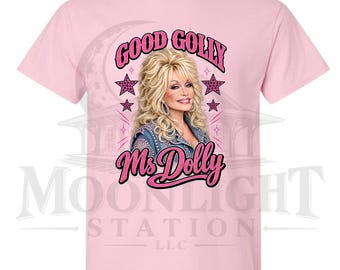 Può includere: Una t-shirt a maniche corte rosa chiaro con la grafica di una donna bionda dai capelli voluminosi che indossa una giacca di jeans. Il testo recita GOOD GOLLY Ms Dolly in lettere rosa, circondato da icone di stelle rosa.