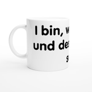 May include: A white ceramic mug with a handle on the left side, featuring black printed text that reads I bin, w und des s.