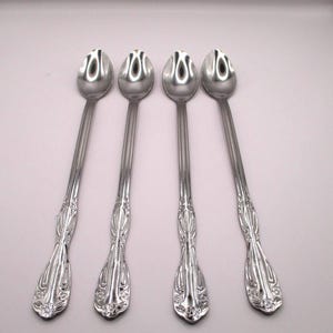 May include: A set of four long-handled silver-toned metal spoons. Each spoon features a polished oval bowl and a slender, elongated stem that transitions into a decorative, embossed handle base with intricate floral-inspired detailing.
