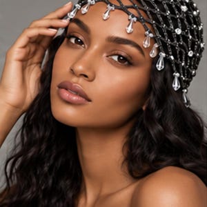 May include: A black net headpiece featuring a lattice pattern adorned with clear, faceted crystals and dangling teardrop-shaped crystal accents that frame the forehead. The accessory is constructed from dark, woven material.