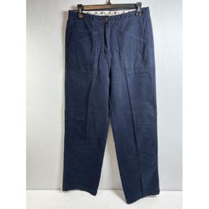 Pode incluir: Calças azul-marinho escuro com design de cintura alta, fecho de botão e braguilha com zíper. Estas calças incluem dois bolsos grandes e angulares na frente e um forro interno branco no cós decorado com um padrão floral preto.