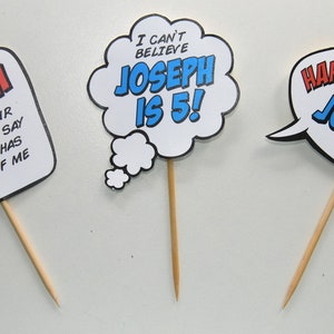 May include: Three colorful comic book style speech bubble cupcake toppers with the text "KABOOM is what your mouth will say after it has a bite of me", "I can't believe Joseph is 5!" and "Happy Birthday Joseph!"