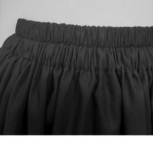 May include: Close-up of a black skirt with an elastic waistband. The fabric is gathered, creating a full, flowing silhouette. The skirt appears to be made of a lightweight material, suitable for various occasions.