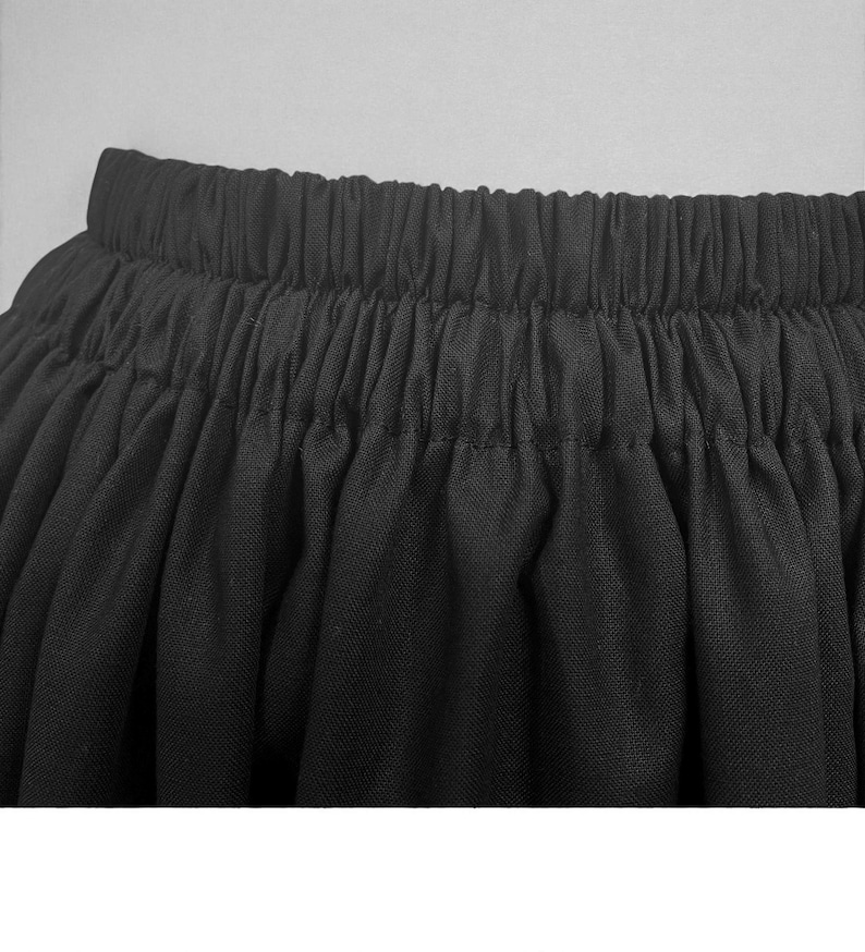 May include: Close-up of a black skirt with an elastic waistband. The fabric is gathered, creating a full, flowing silhouette. The skirt appears to be made of a lightweight material, suitable for various occasions.
