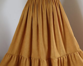 May include: A mustard yellow skirt with a gathered waist and multiple tiers of ruffles. The skirt is made of a soft, textured fabric.