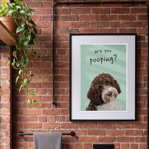Puede incluir: Una lámina de pared enmarcada que muestra un perro marrón y blanco sobre un fondo verde claro con el texto are you pooping? escrito en letras negras sobre la cabeza del perro. La lámina tiene un marco negro sencillo con paspartú blanco.