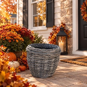 May include: A round, woven planter with a dark gray, weathered finish and a thick, braided rim. The planter features a deep, open interior and a tapered base, constructed from synthetic material designed to mimic natural wicker texture.
