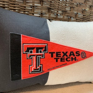 May include: A black and white pillow with a red and white pennant featuring the Texas Tech logo and the text "Texas Tech" and "RICO INC./TAG EXPRESS".