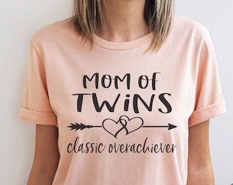 May include: A pink t-shirt with the text "Mom of Twins classic overachiever" and an arrow with a heart design.