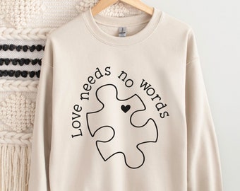 May include: A beige sweatshirt with a black puzzle piece design and the text "Love needs no words".