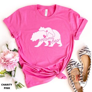 May include: A bright pink t-shirt with a white graphic of a mama bear and cub, with the words "mama bear" in script. The shirt is folded and has the words "Charity Pink" at the bottom.