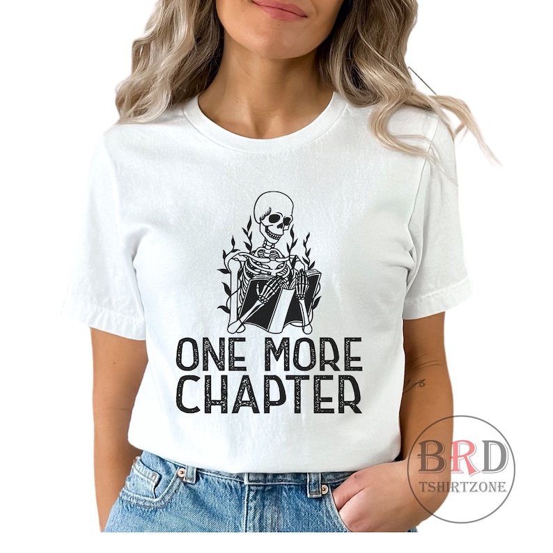 May include: White t-shirt with a black and white illustration of a skeleton reading a book. The text "ONE MORE CHAPTER" is printed below the illustration.
