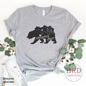 May include: Athletic heather gray t-shirt featuring a black graphic of a mama bear with three cubs. The words "mama bear" are written in a script font. The shirt is styled with white sneakers and cotton sprigs.