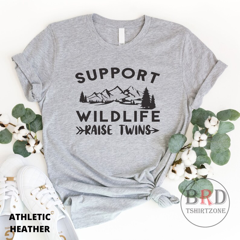 Puede incluir: Camiseta gris con el texto "Support Wildlife >>Raise Twins<<" en negro. El texto est&aacute; rodeado por un gr&aacute;fico de monta&ntilde;as y &aacute;rboles.